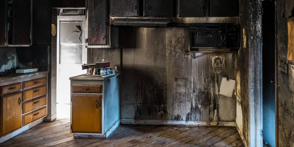 Kitchen with cabinets and walls blackened by fire and smoke